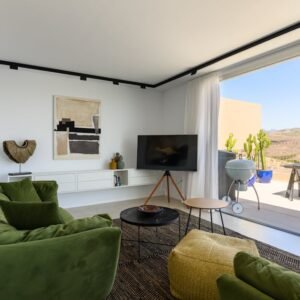 Stylish modern living room with green couches and outdoor balcony overlooking scenic mountains.