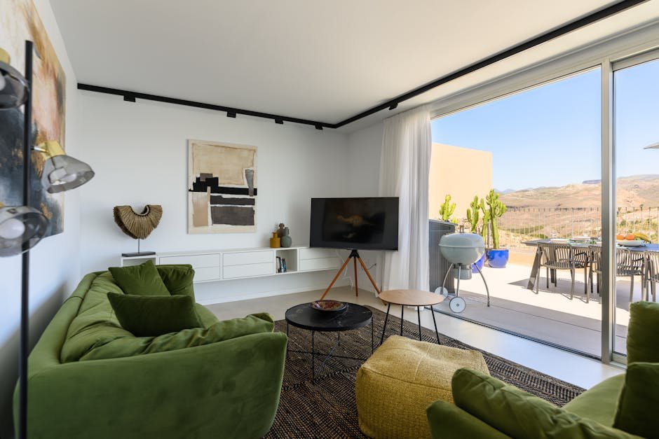 Stylish modern living room with green couches and outdoor balcony overlooking scenic mountains.