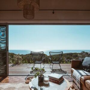 Interior design of luxurious apartment with large balcony doors and wooden terrace having picturesque view on green forested seashore and calm blue sea